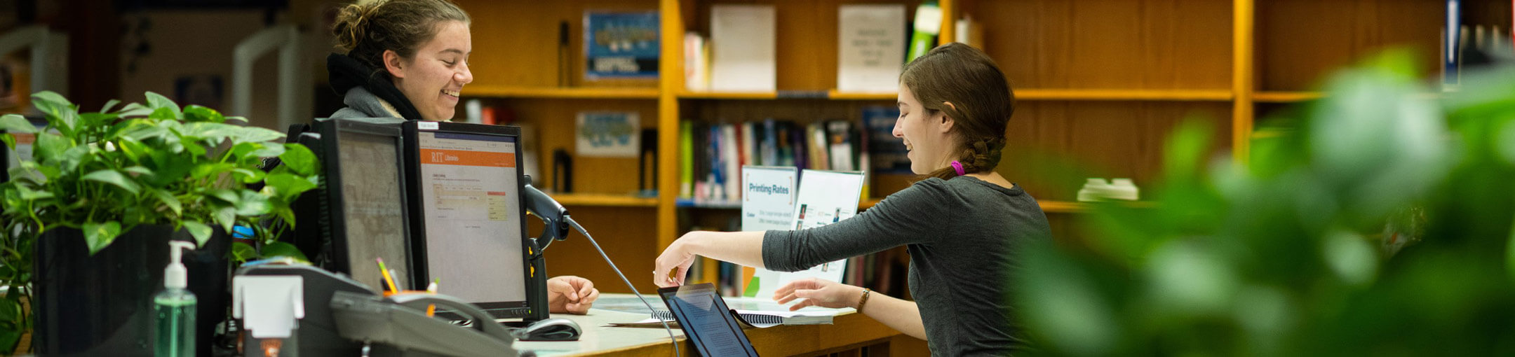 An RIT student employee helping a fellow student in the library