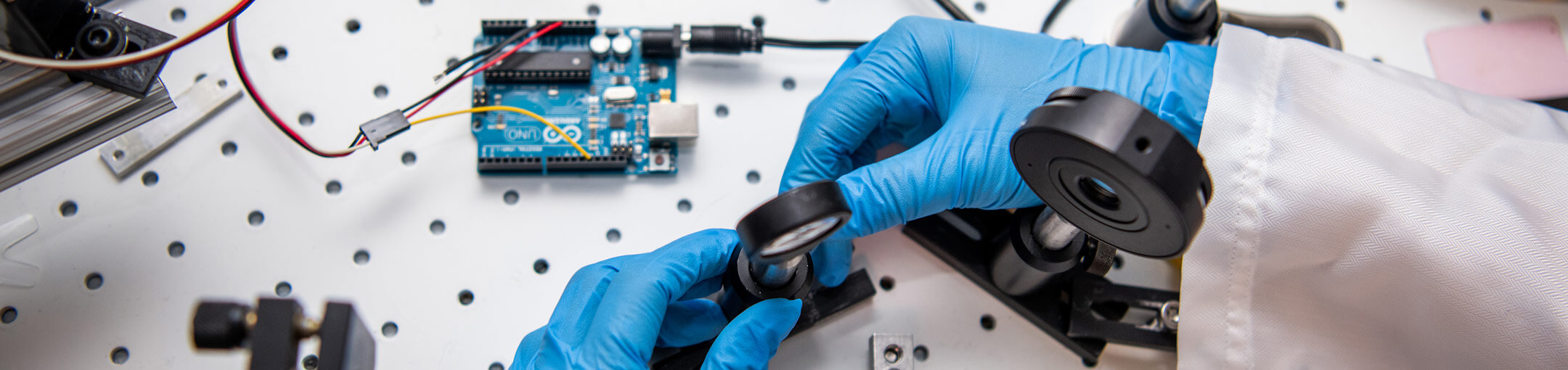 A close up of a researcher's hands adjusting a sensor on a work bench.
