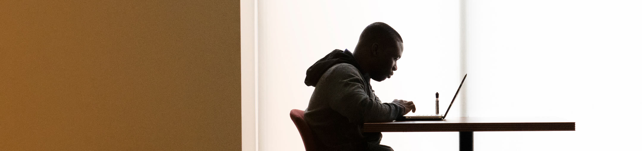 An RIT student sitting at a table working on a laptop.