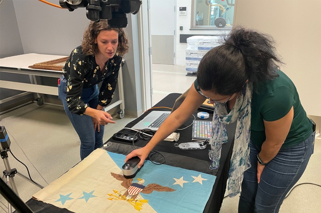two people using a handheld scanner on a fabric flag with a bald eagle.