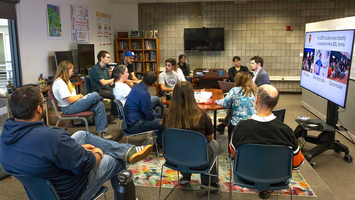 a group of faculty members listening to a presentation in a small gathering space.