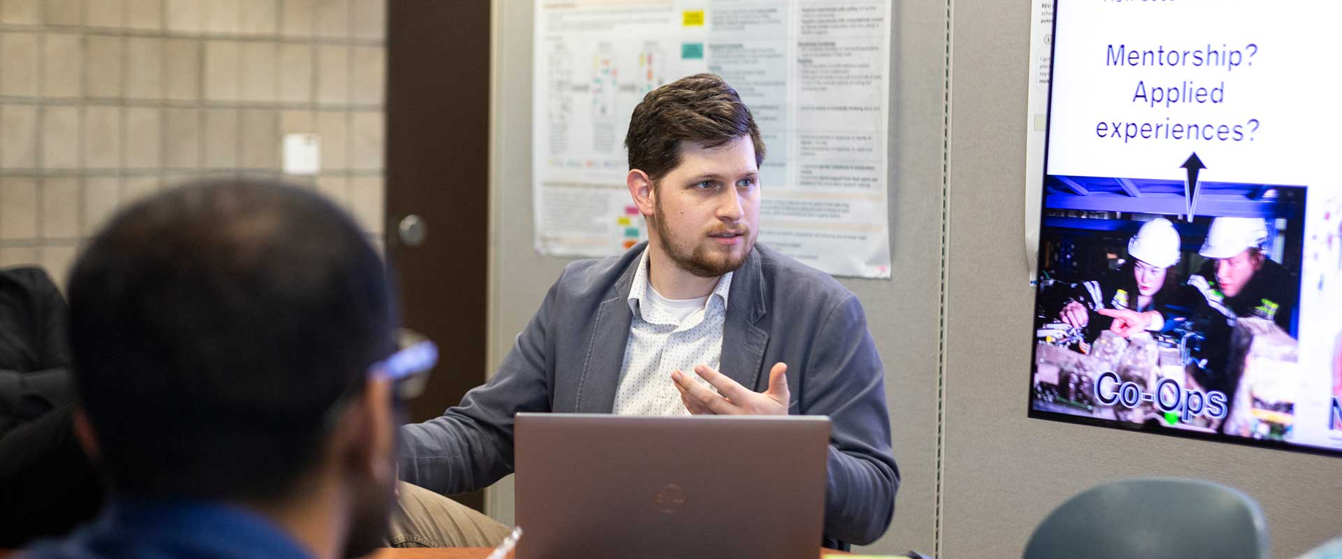 a person giving a presentation while seated, with a projection screen in the background.