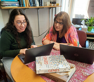 Deanna Abid and Dr. Dina Newman sitting at a table, working on their laptops.