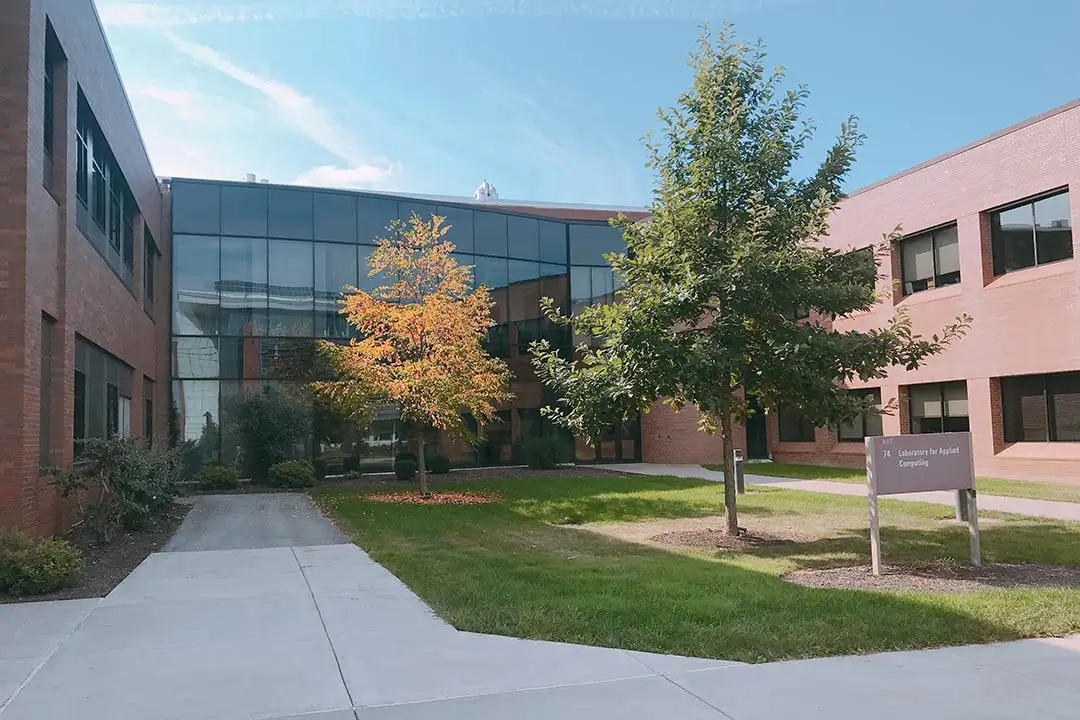 Two brick buildings connected by an enclosed glass walkway, with a small courtyard.