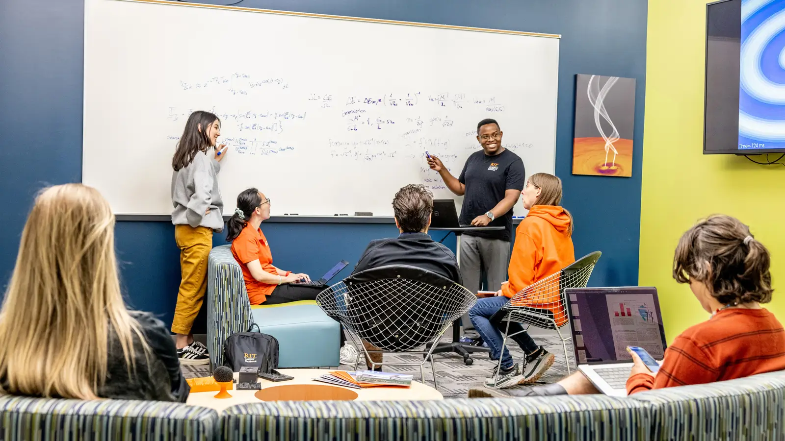 A group of students gathered in the meeting area, working on equations and having a discussion.
