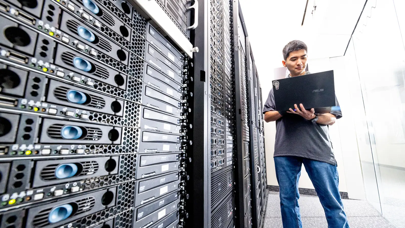 A researcher standing next to a supercomputer, holding a laptop.