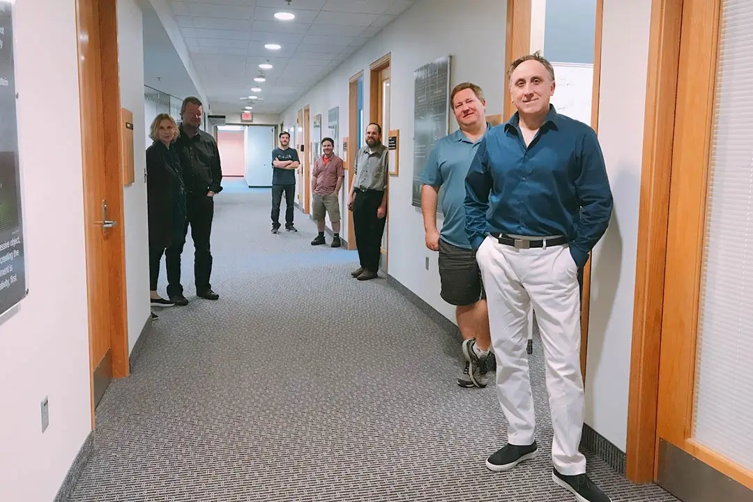 View down a hallway of offices, with the office occupants standing outside their doors.