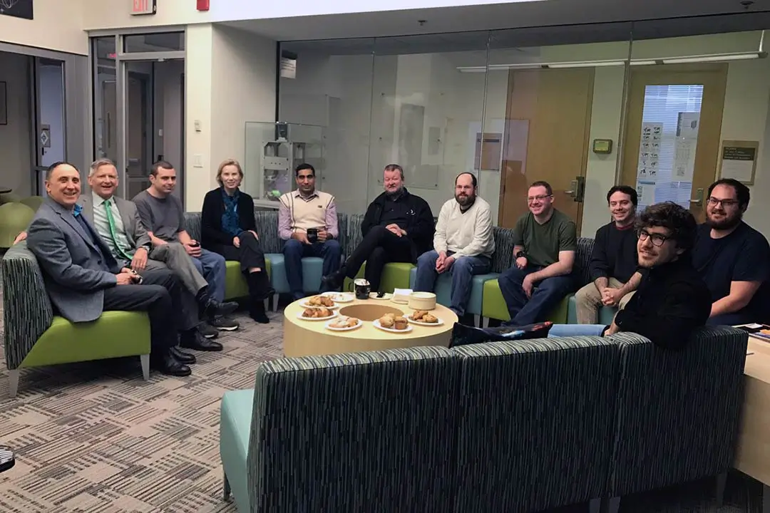 A group of faculty and students sitting on a sectional sofa in a lounge.
