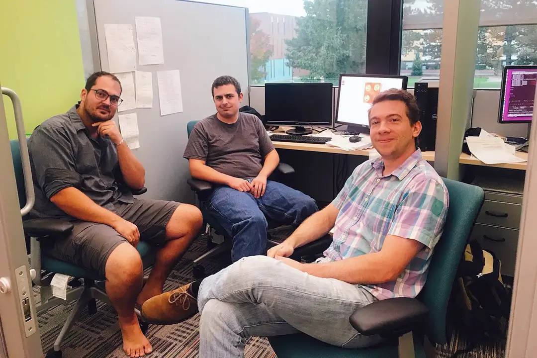A cubicle-style office space with three student workers.