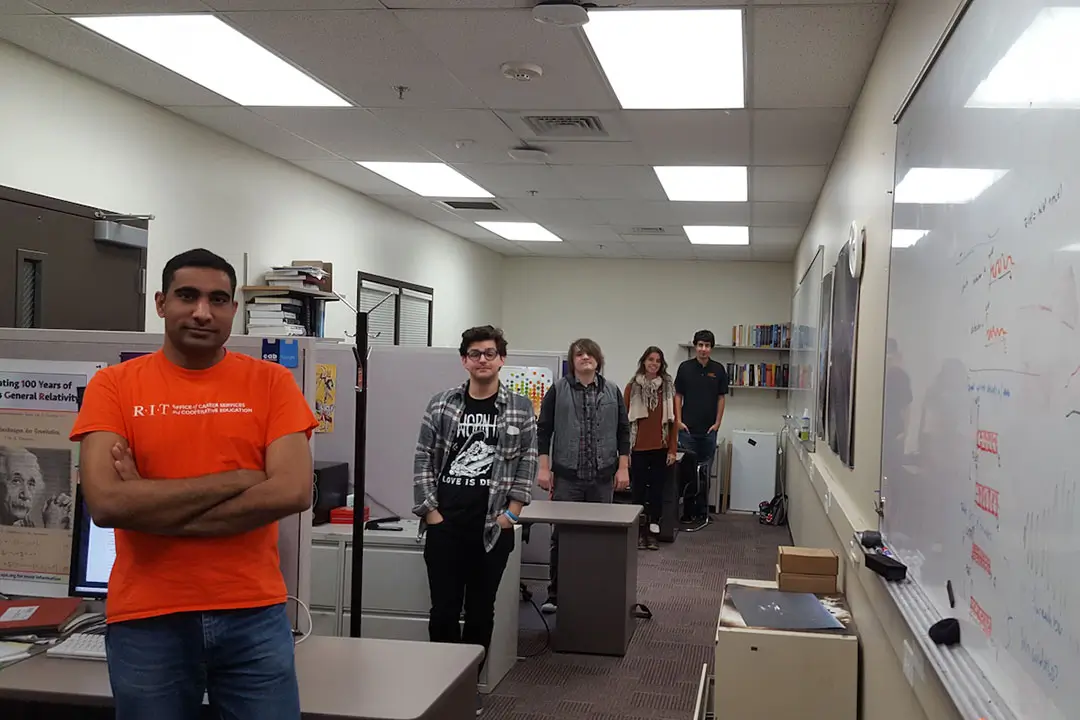 A long office space with students standing outside their workspaces.