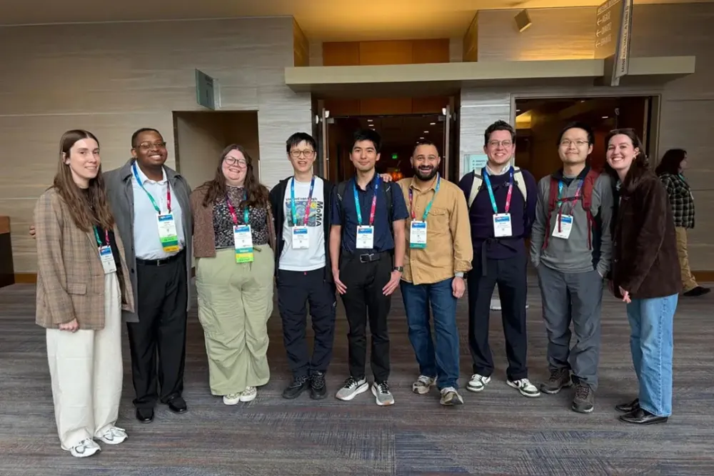 A group of nine people wearing I D lanyards poses for a photo.