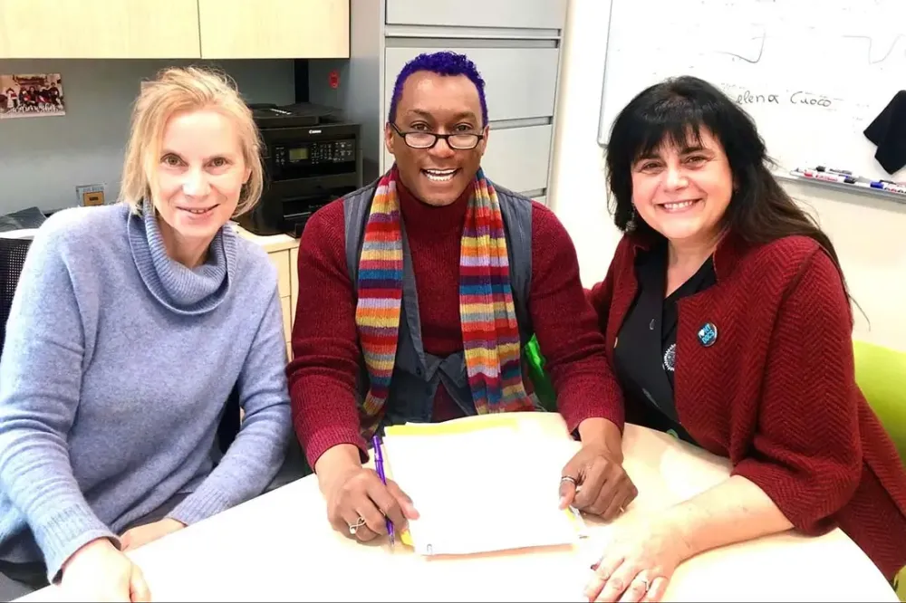 Three people sitting at a table, with the center person holding a script.