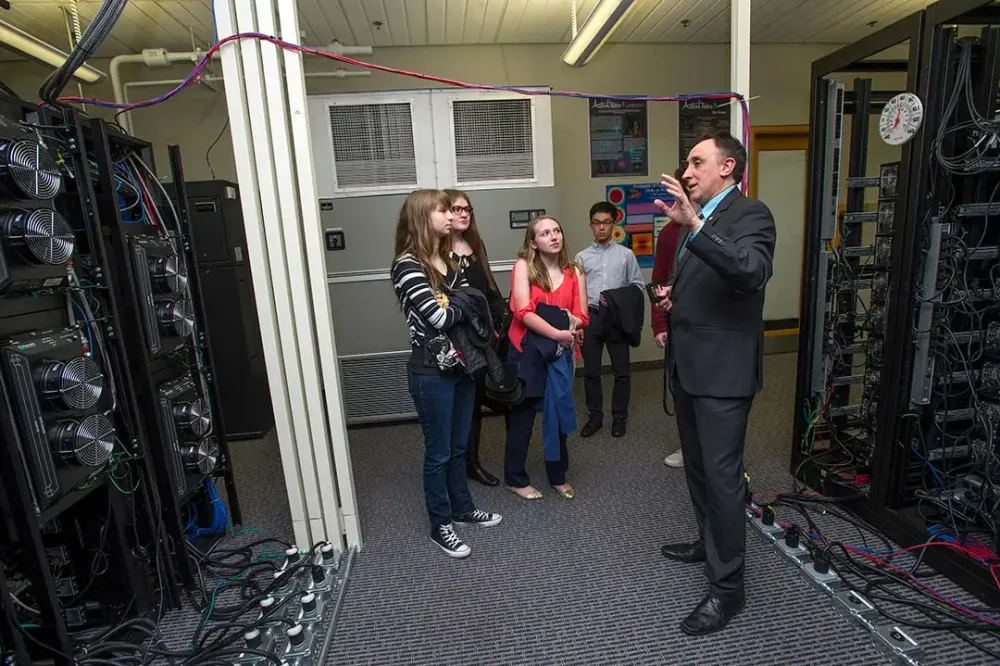 A professor speaks in a server room while a small group of students listens.