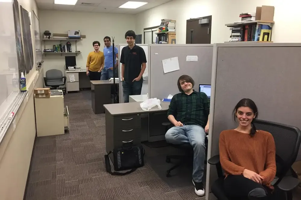 Student workers stand or sit next to their office spaces.