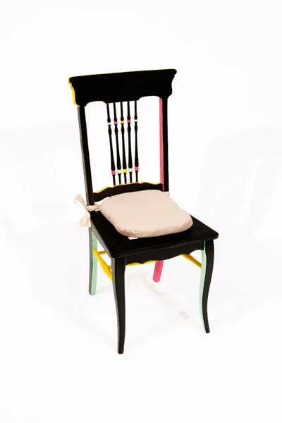 A black chair with pink, yellow, and green painted on the underside of the chair. A pink tie able cushion for the seat. 