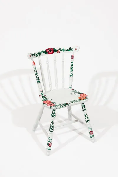This chair is a wooden chair painted white, and painted with light colored flowers and leaves.