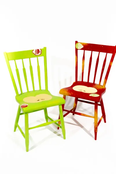 Two chairs painted to look like apples with produce stickers. One red and one green.