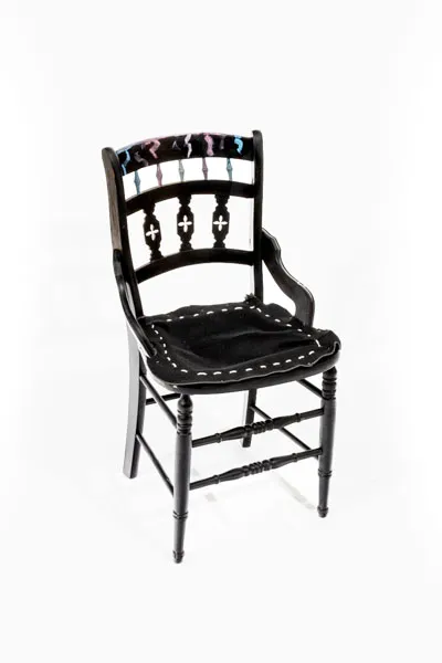 Black chair with moles/critters painted on it. The seat is a layer of fabric stitched into the chair with white rope