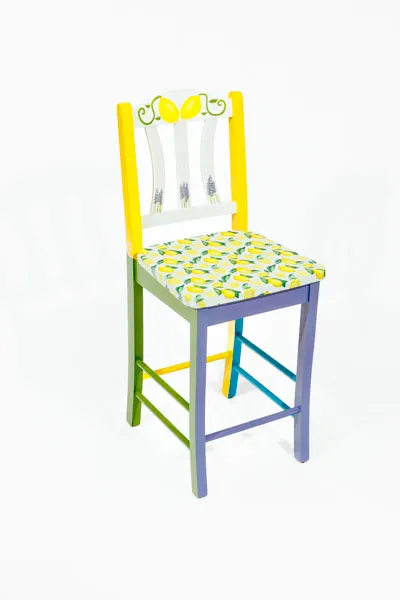 Chair with lemons and lavender painted painted on the back. The seat has lemons on it as well. The legs are painted green, purple, blue, and yellow. 