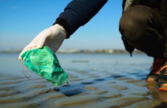 gloved hand picking up discarded face mask in a body of water