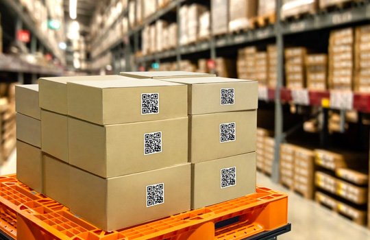 QR codes on a stack of brown cardboard boxes in a warehouse