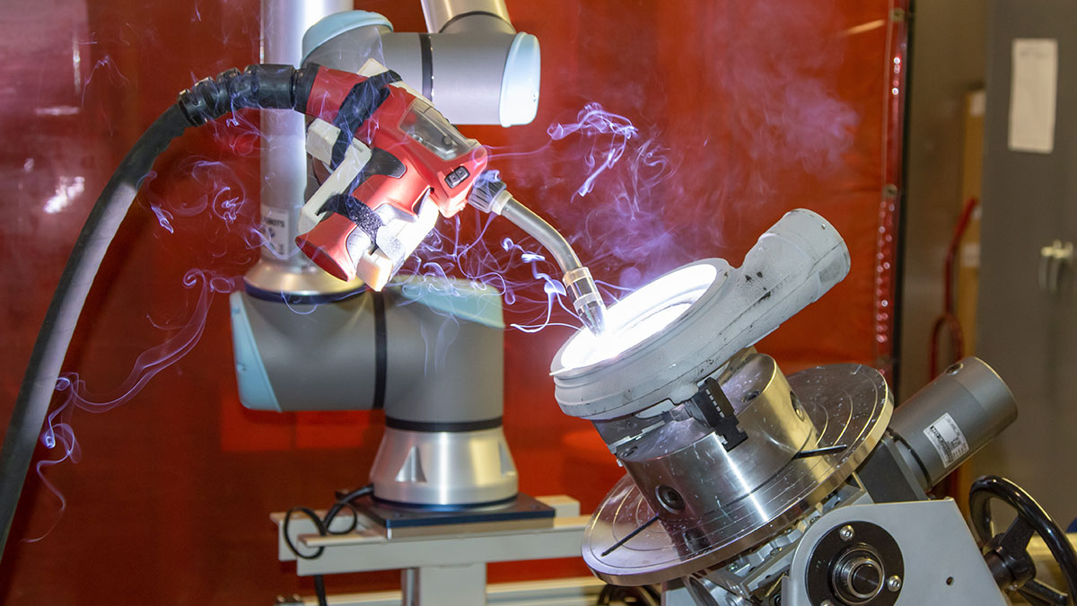 A robotic welding arm operating on a metal component in an advanced manufacturing lab.