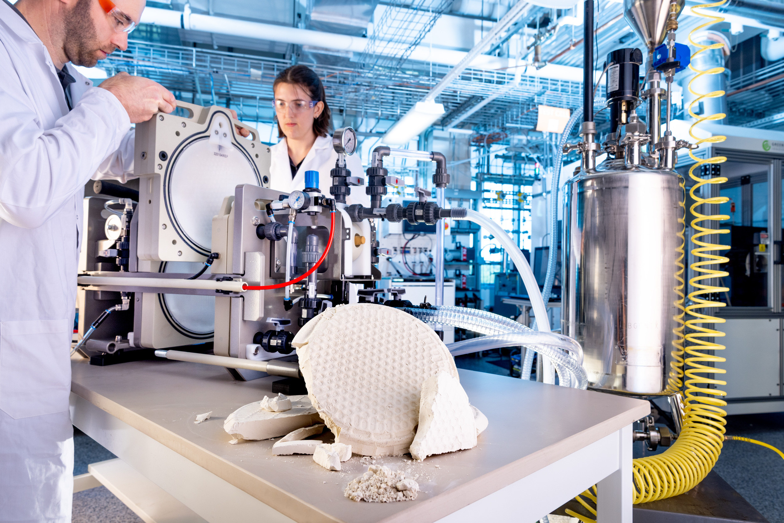 Two engineers in a lab wearing white lab coats working on a machine