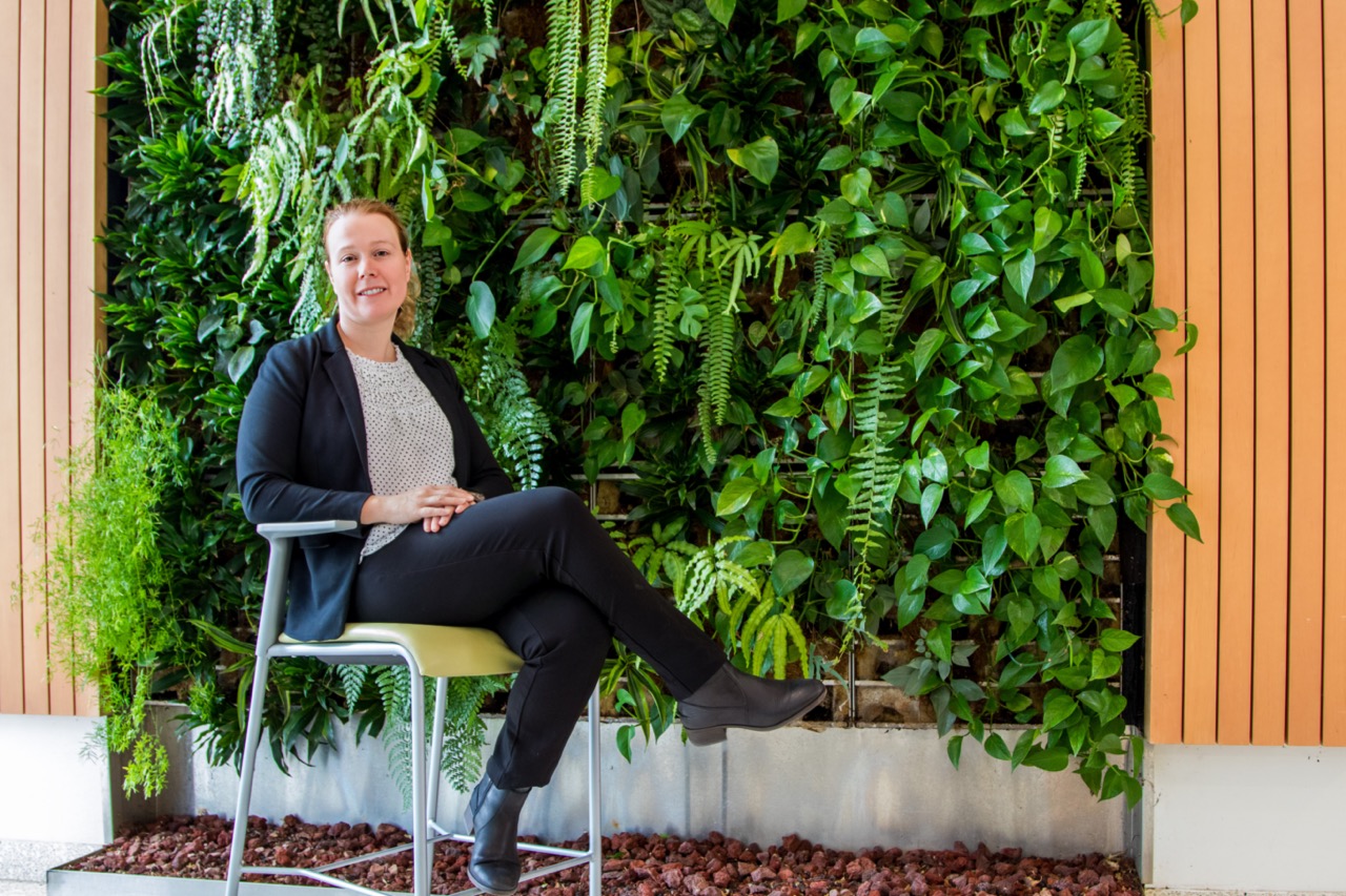 Annick Anctil sitting on a chair in front of the green living plant wall in the GIS building