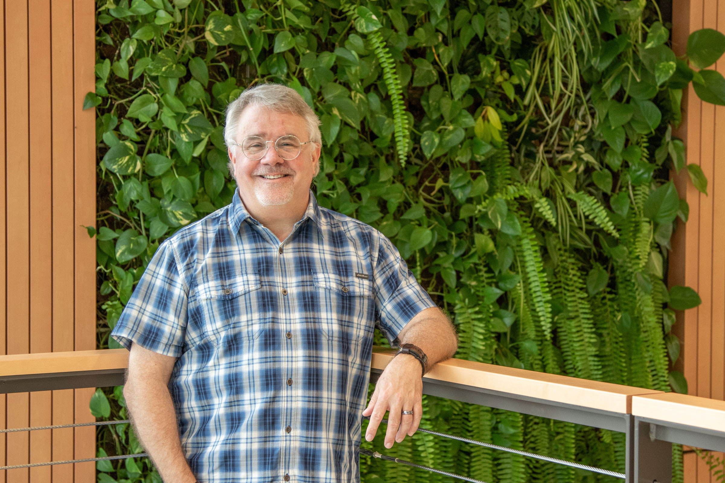 John Warner leaning on railing while standing in front of the green living plant wall in the GIS building
