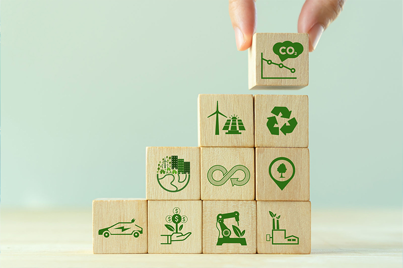 Hand stacking wooden blocks with different icons representing circular economy and life cycle assessment on a light green background