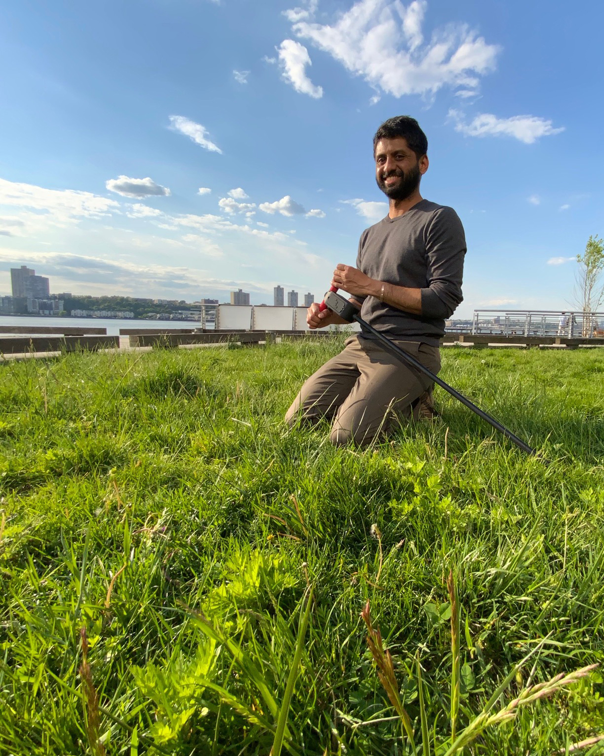 Man kneeling in field holding a smart sensor compost system while kneeling in a grass field
