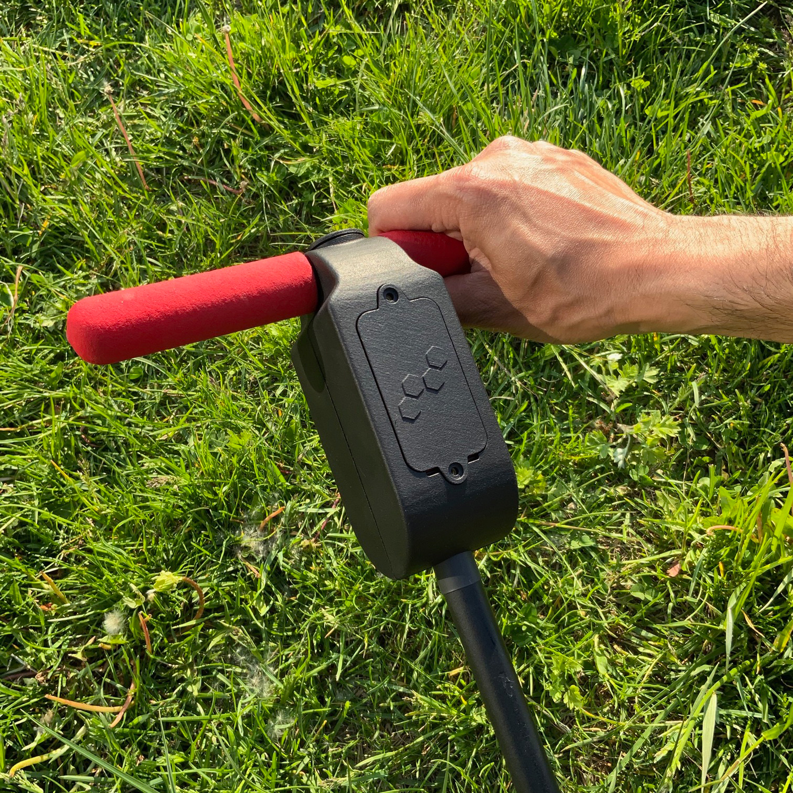 Hand holding a smart sensor compost system over a bed of grass
