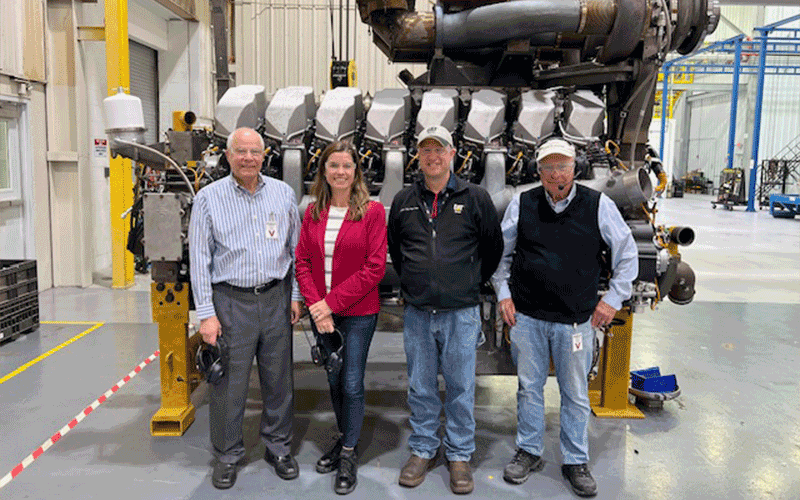four people standing in front of large engine