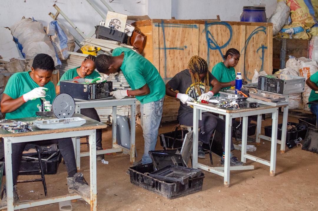 people in green tshirts wearing safety gloves working at station to disassemble various types of electronics