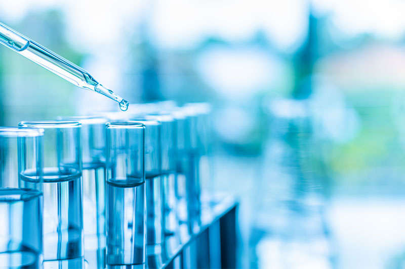 clear test tubes with clear dropper dropping clear liquid on a blurred background of blues and greens