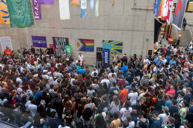 crowd of people listening to a speaker at a podium outside.