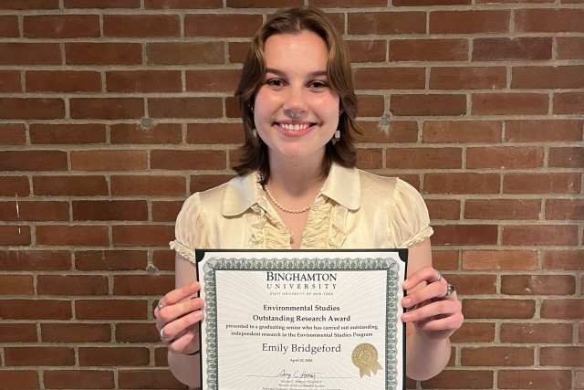 A woman stands in front of brick wall holding an award plaque