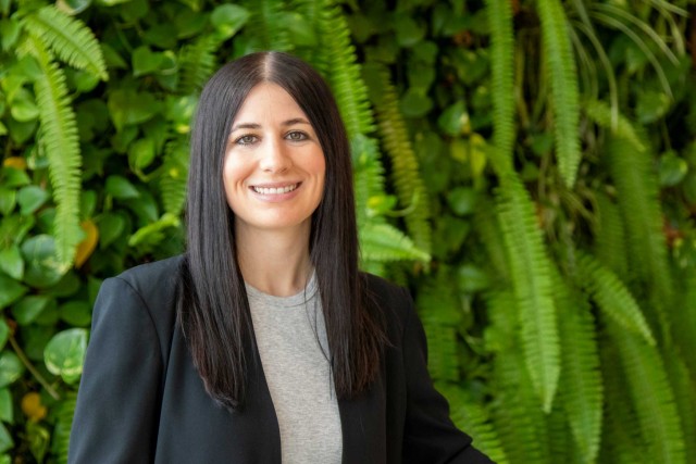 An image of Amanda Reis, an RIT faculty member, before a wall of green foliage