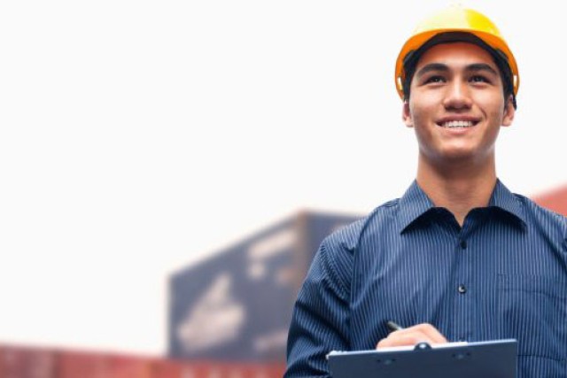 a man in a yellow construction hat writes on a clipboard.