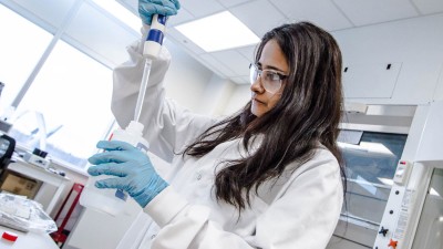 Woman in goggles and lab coat, squeezing a liquid in a bottle.