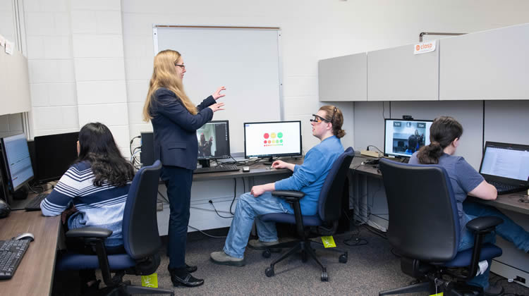 Professor Alm speaking with several students in a lab.