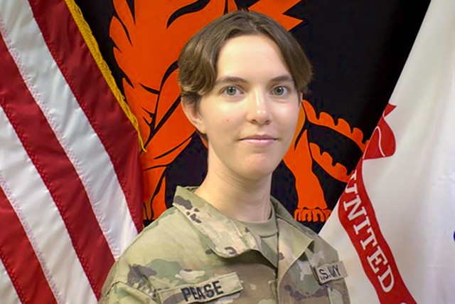 a woman with short brown hair sits in front of the american and R O T C flags