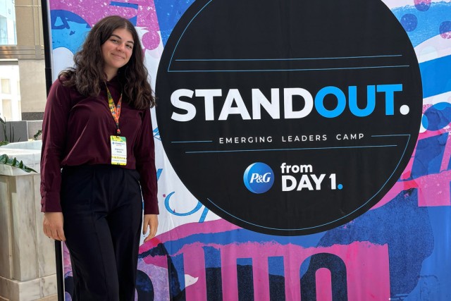 a college age woman stands next to a poster for Stand Out Emerging Leaders camp