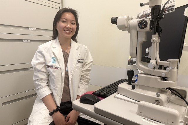 Melanie Ng poses next to ophthalmic imaging equipment at Massachusetts Eye and Ear Infirmary, where she began working shortly after graduating from RIT's photographic sciences program in 2026.