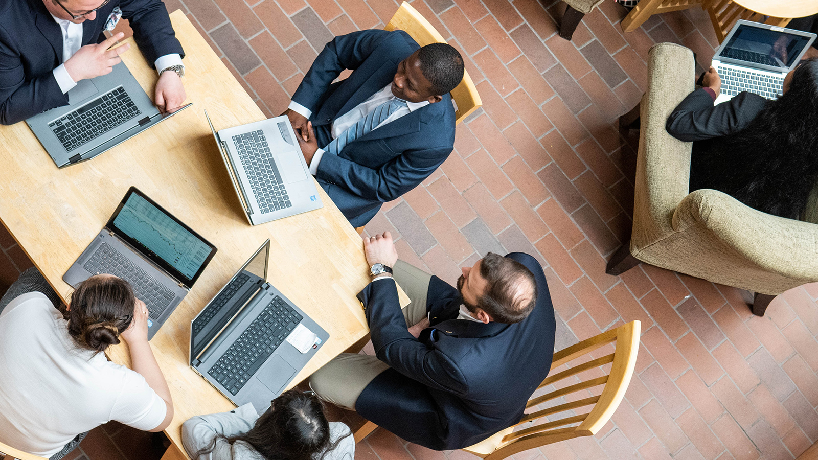Four individuals seated around a table, each working on their own laptop in a well-lit indoor space, suggesting a collaborative work environment.