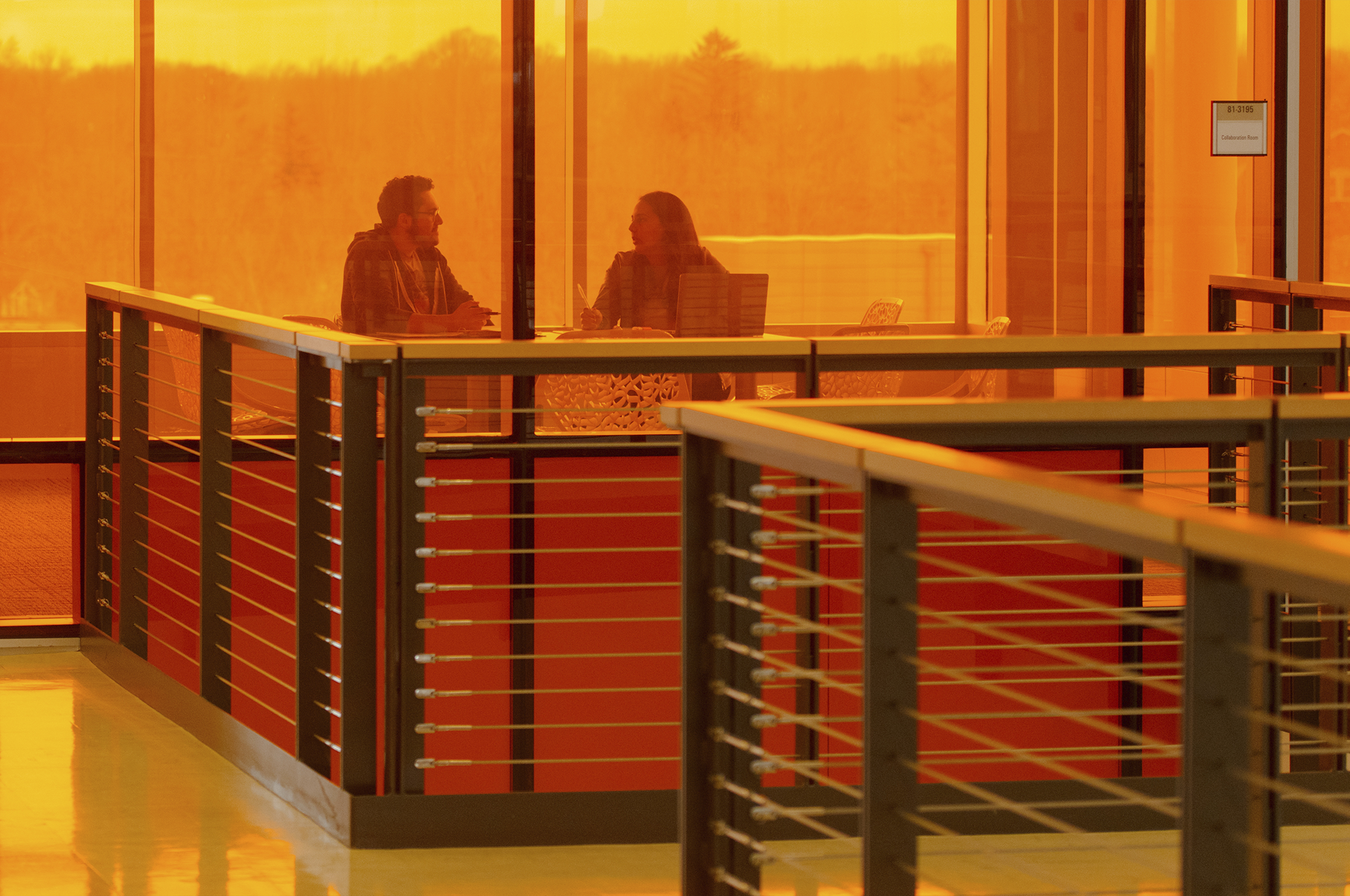 Two people talking in a room behind orange glass.