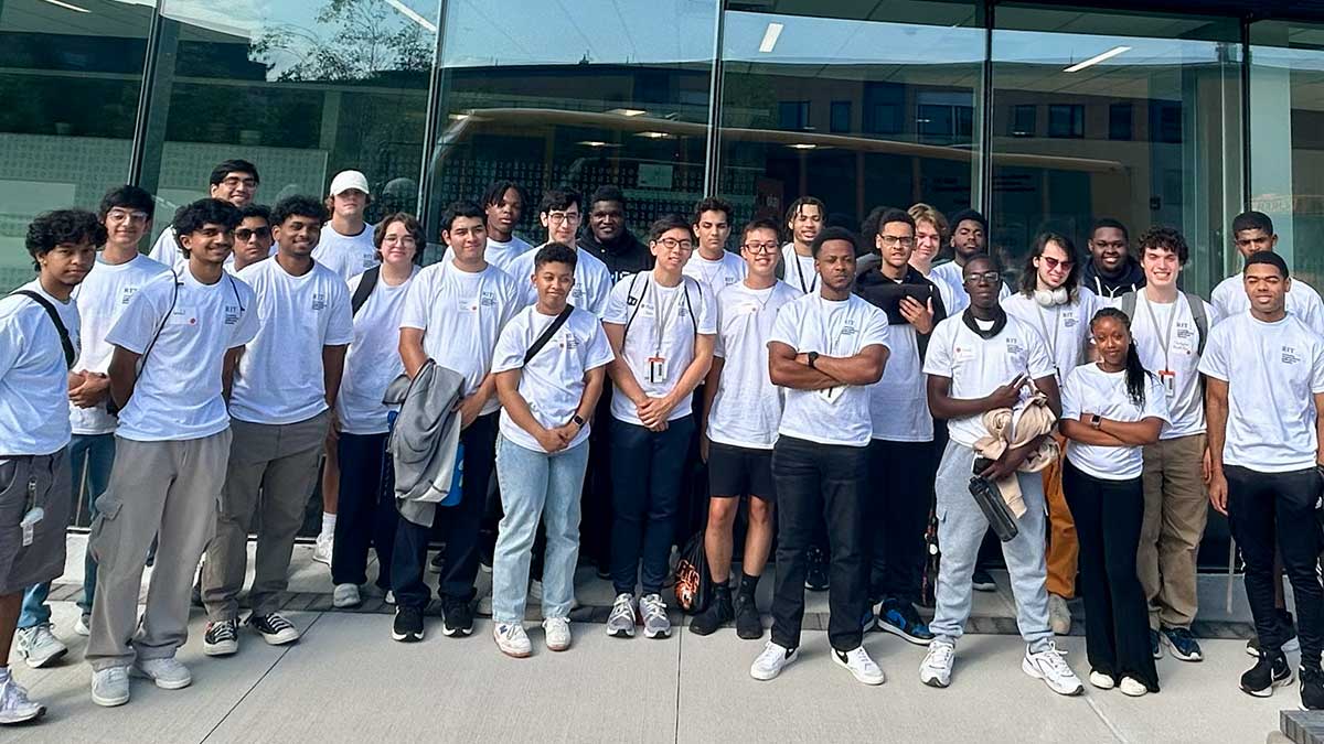 a large group of diverse students wearing matching white T-shirts poses for a photo outdoors.