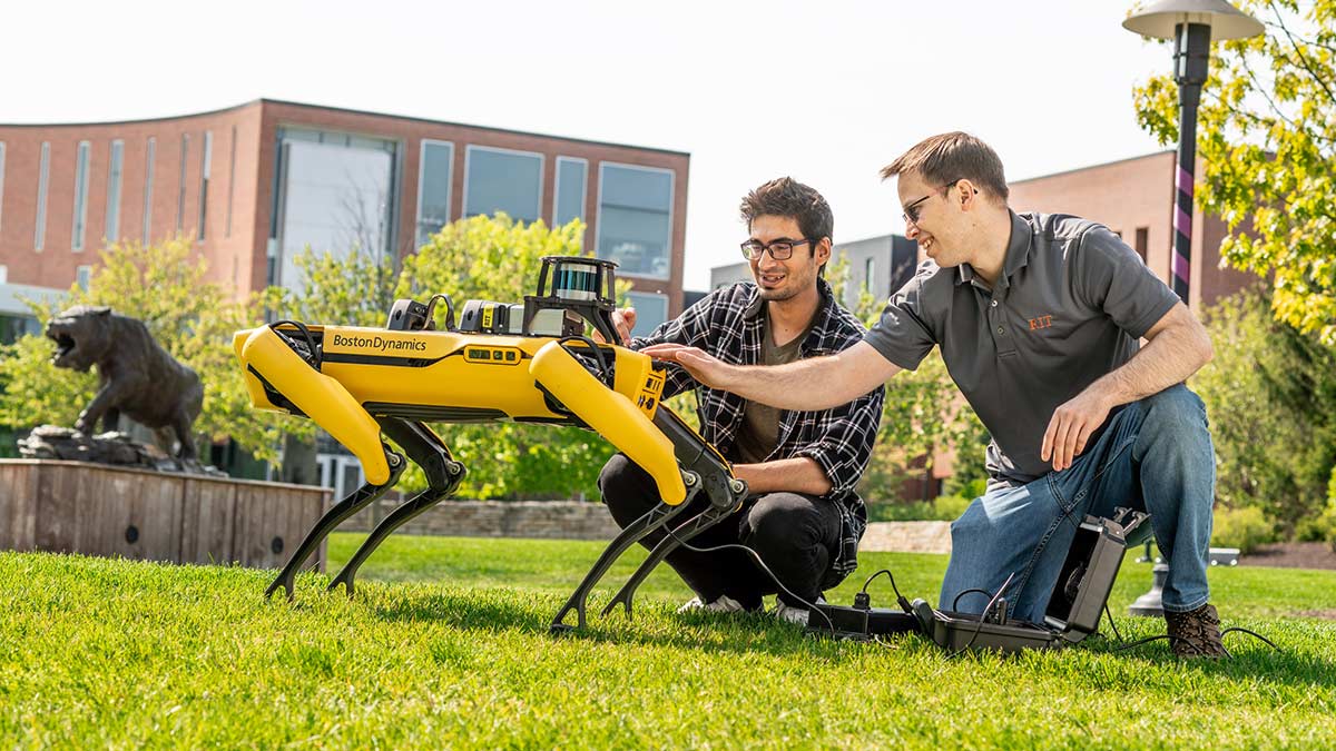 two people are interacting with a Boston Dynamics robot outdoors on campus.