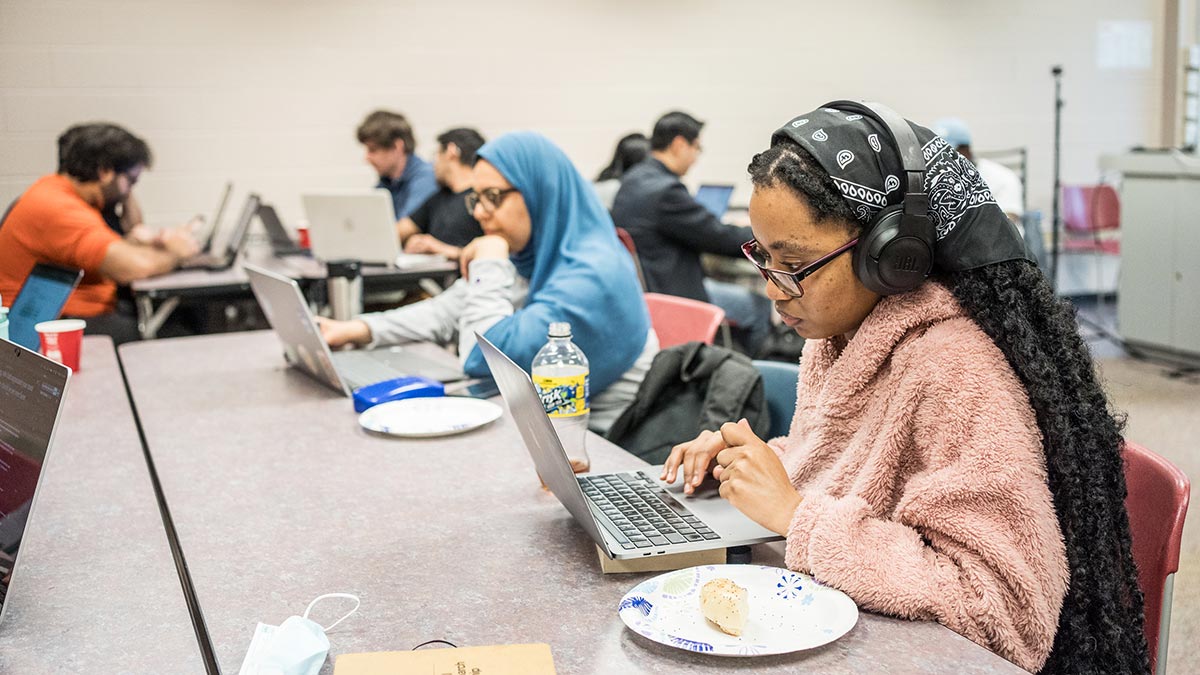 students sit at tables working on their laptops as part of a hackathon.