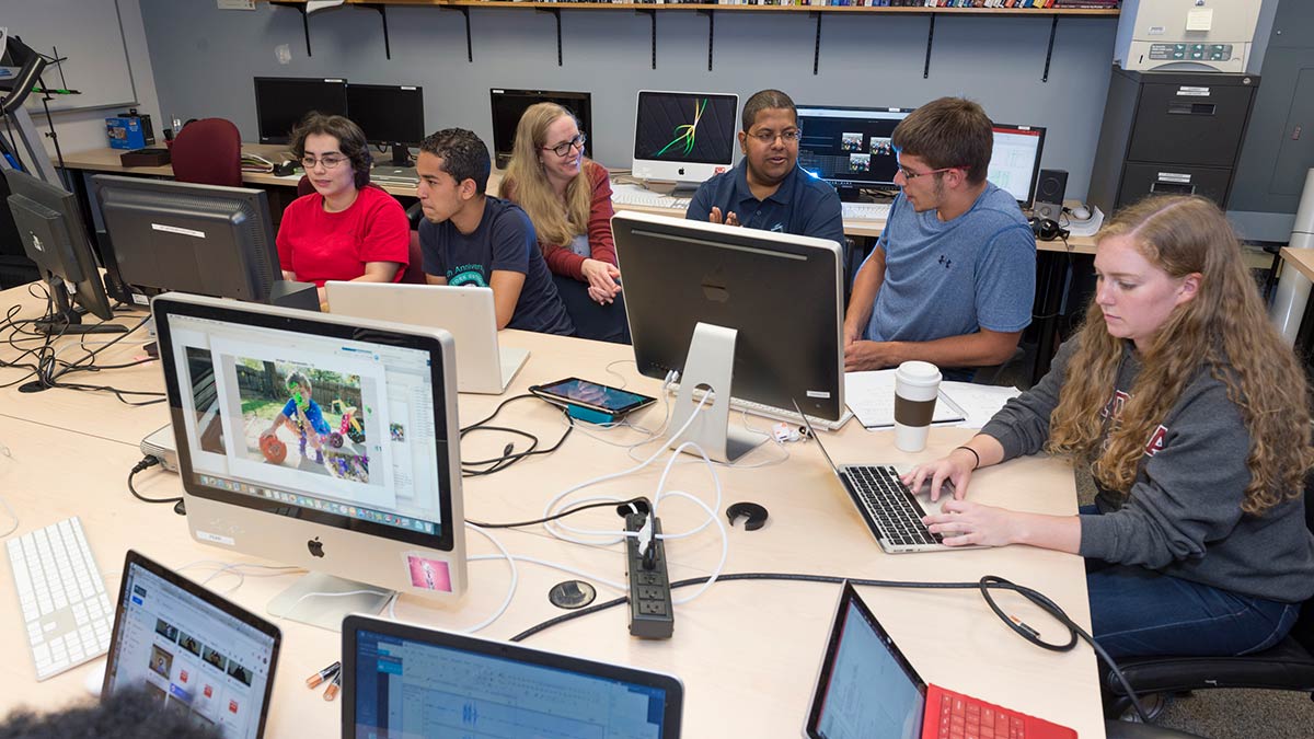 four students and two professors sitting around a table working on computers.